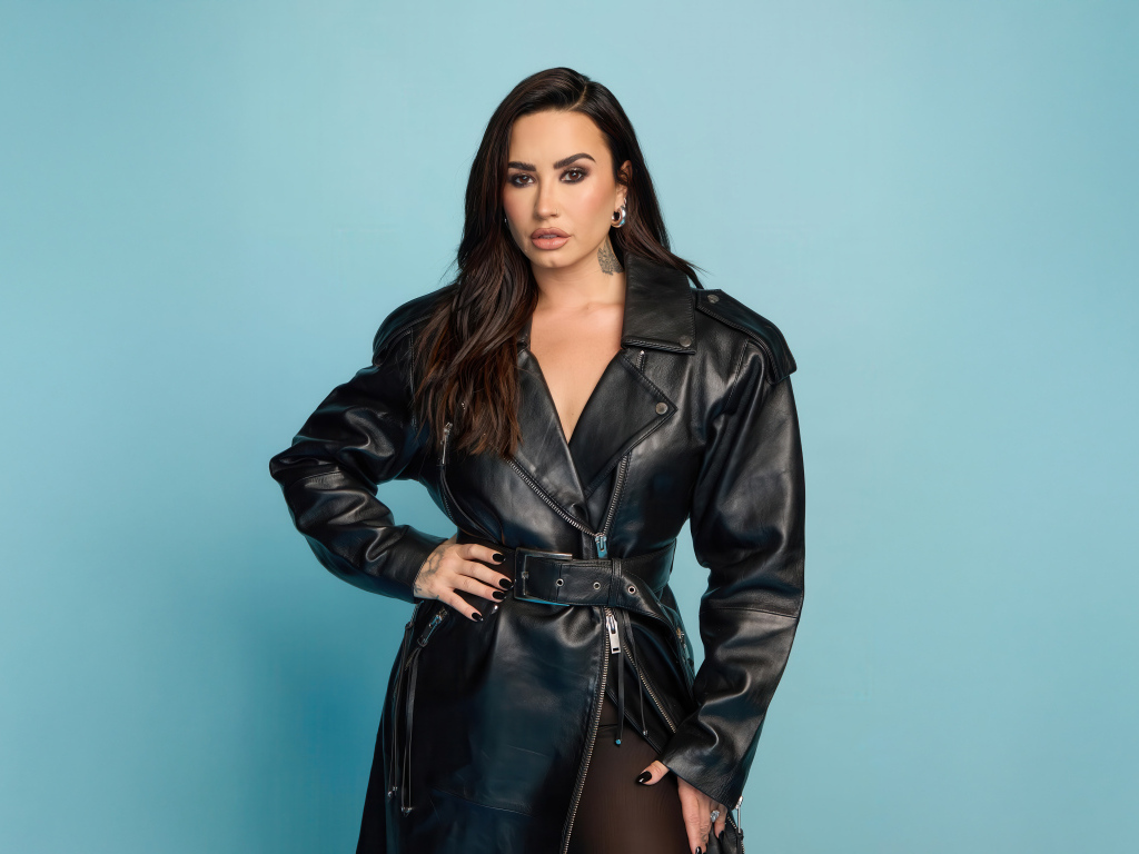 Певица Деми Ловато в кожаном черном пальто на голубом фоне