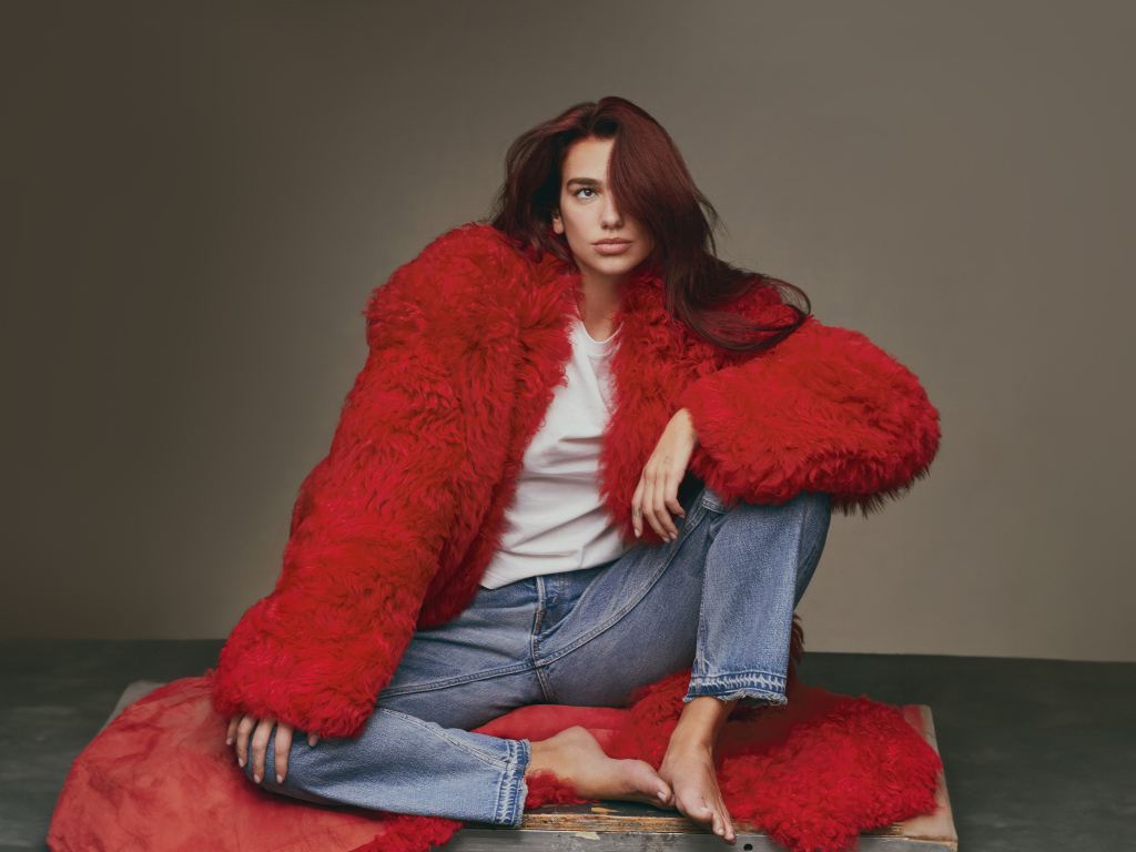 Певица Дуа Липа в красной шубе сидит на полу