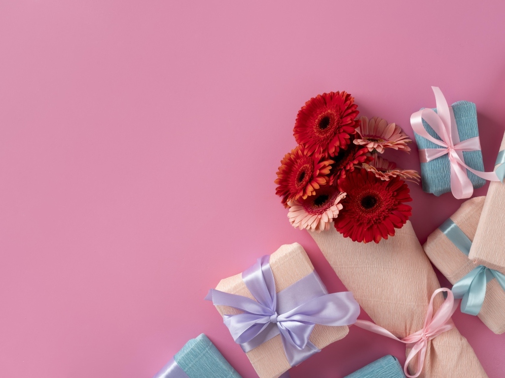 Букет цветов герберы с подарками на розовом фоне