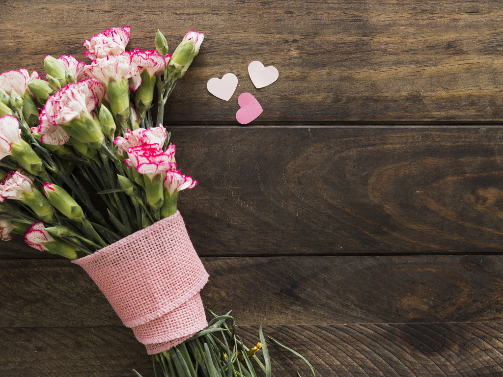 Розовые гвоздики с сердечками на коричневом деревянном фоне