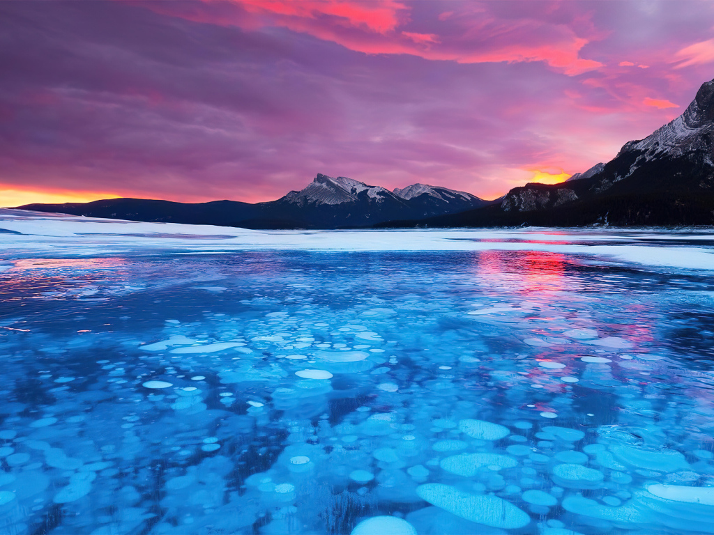 Красный закат солнца над горами у покрытого льдом озера