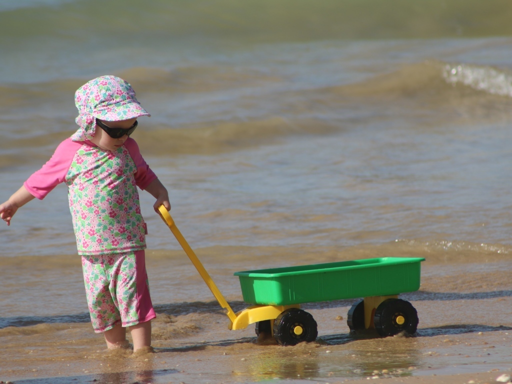 Девочка с машинкой играет на песке у моря
