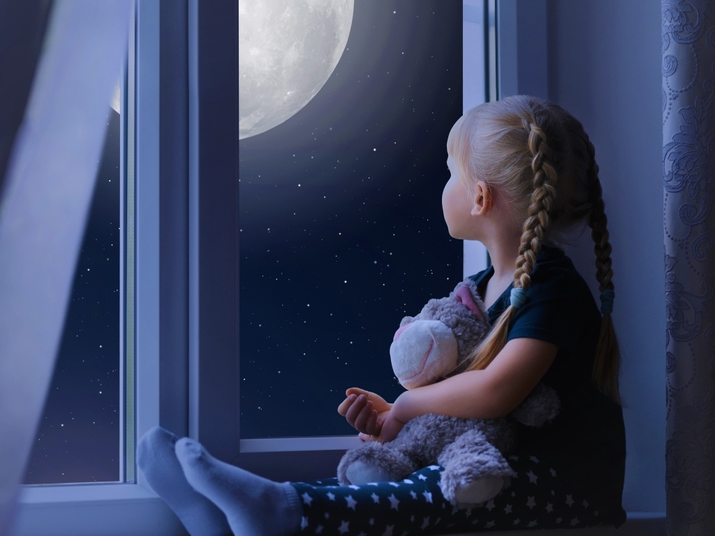 Маленькая девочка с игрушкой смотрит у окна на луну