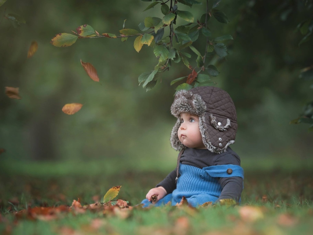 Карапуз в шапке сидит под деревом осенью