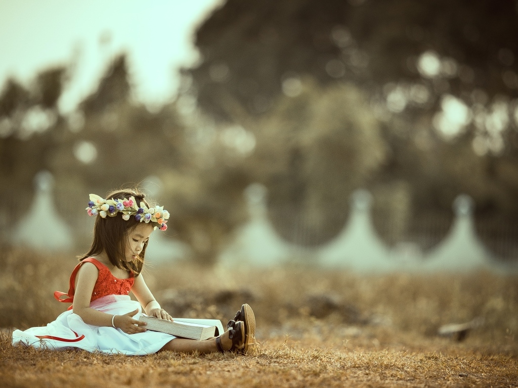 Девочка азиатка сидит с книгой на земле