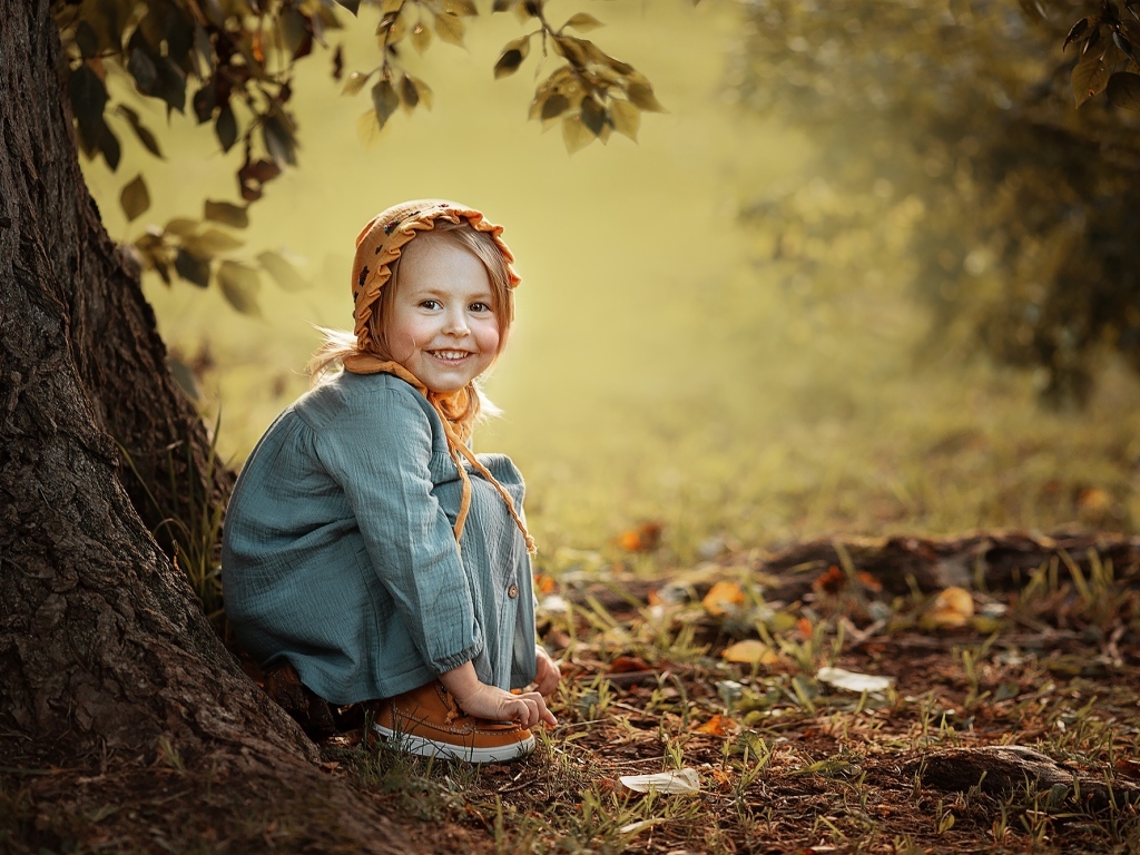 Красивая улыбающаяся девочка сидит под деревом