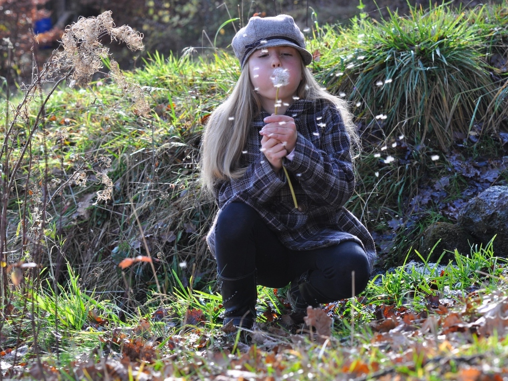 Девочка в кепке дует на одуванчик