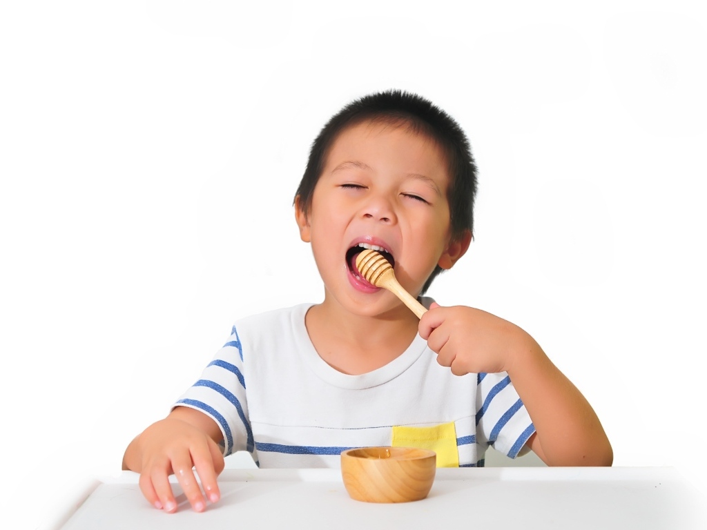 Маленький мальчик ест мед на белом фоне
