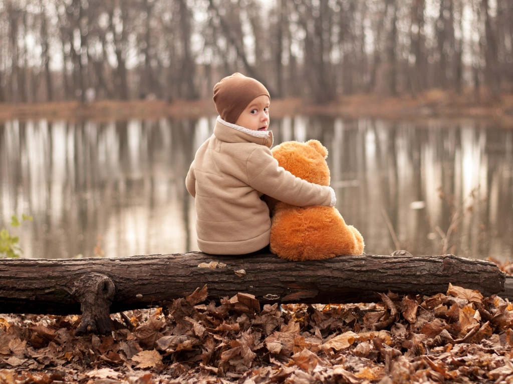 Маленький мальчик с игрушкой сидят на колоде у озера осенью
