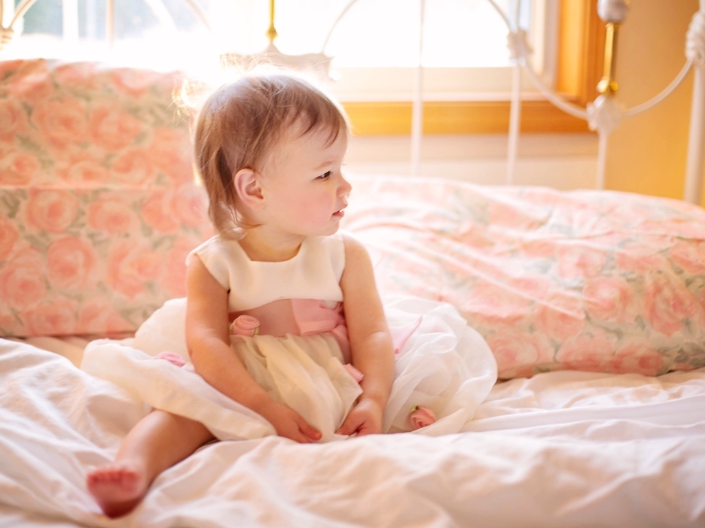 Маленькая девочка в платье сидит на кровати