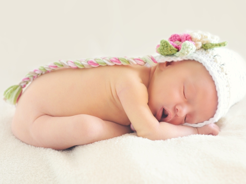 Спящая новорожденная девочка с вязаной шапке
