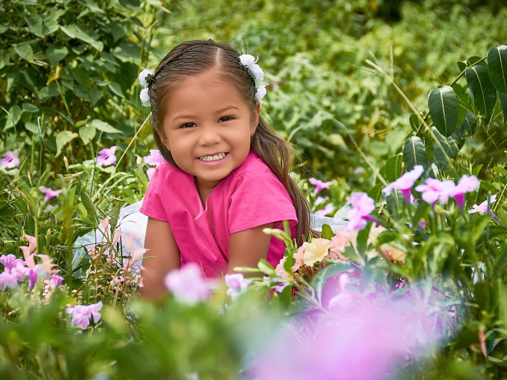 Улыбающаяся маленькая девочка сидит в цветах