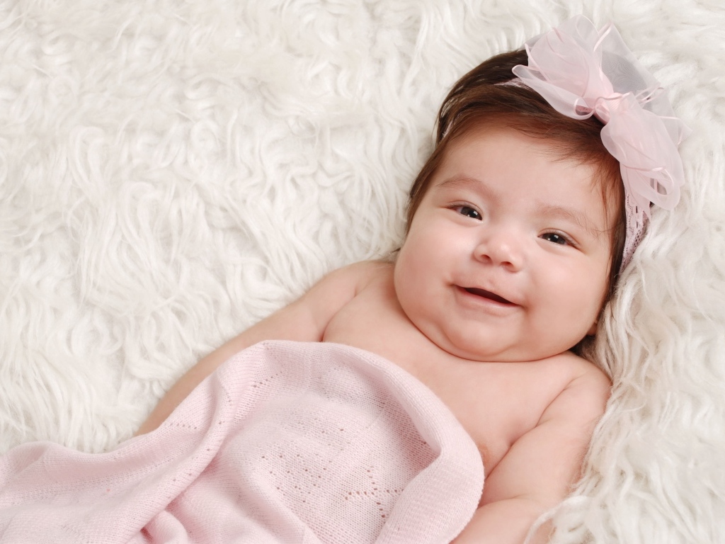 Улыбающаяся новорожденная малышка с бантом на голове