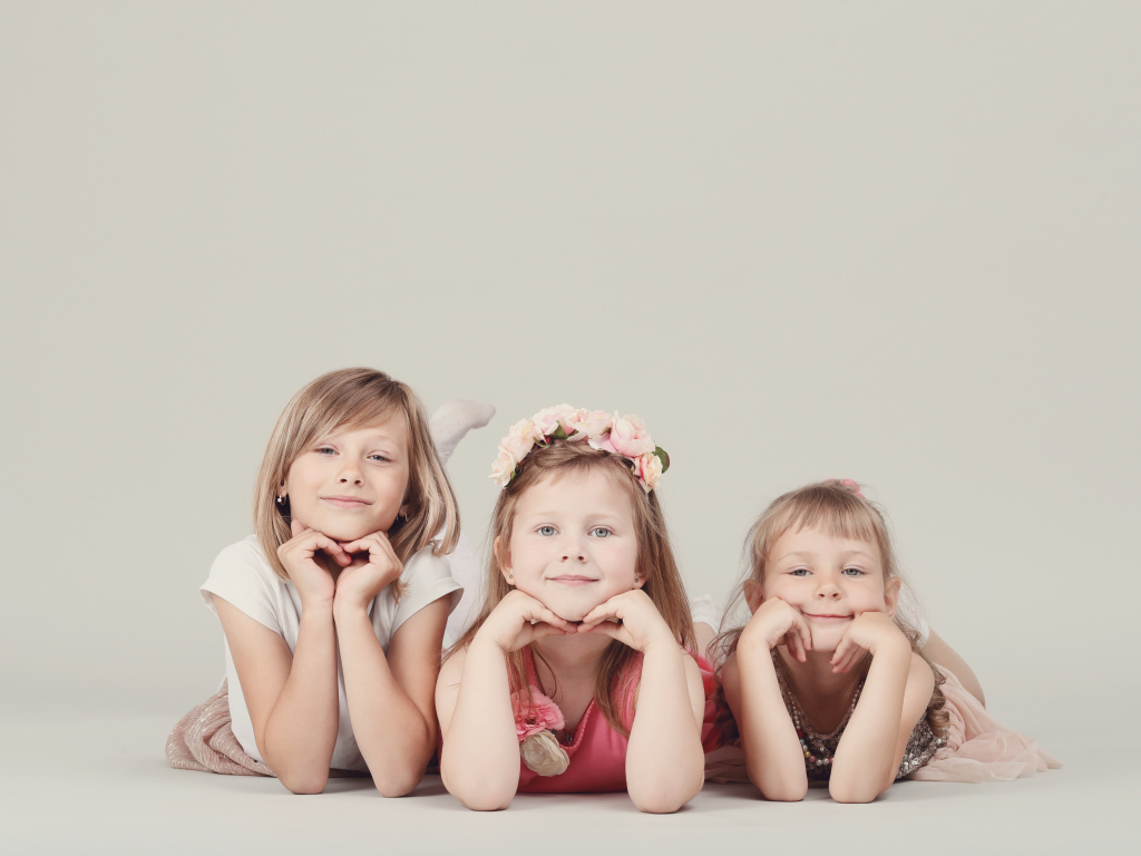 Три маленькие девочки лежат на сером фоне