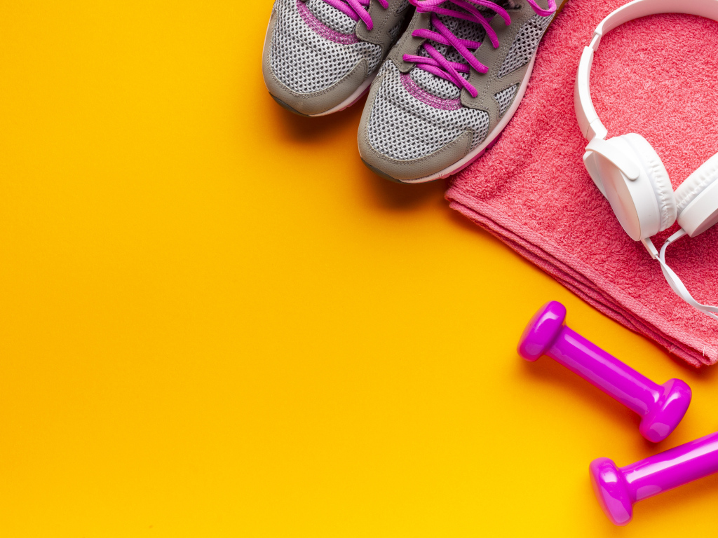 Розовые гантели, наушники, кроссовки и полотенце на желтом фоне