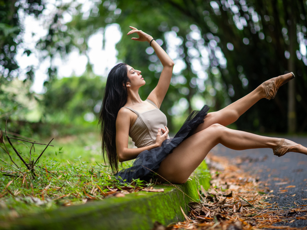 Девушка балерина в короткой юбке сидит на земле