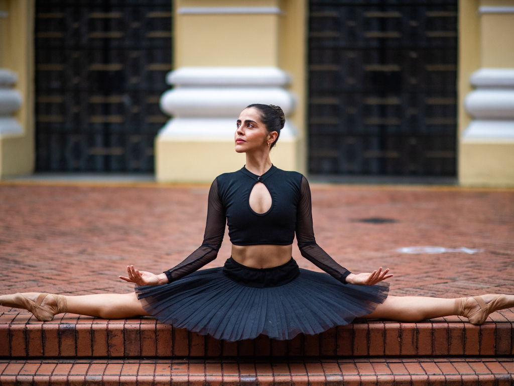 Девушка балерина в черном сидит на шпагате