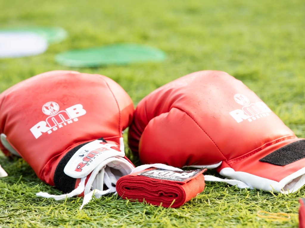 Красные боксерские перчатки лежат на зеленой траве 