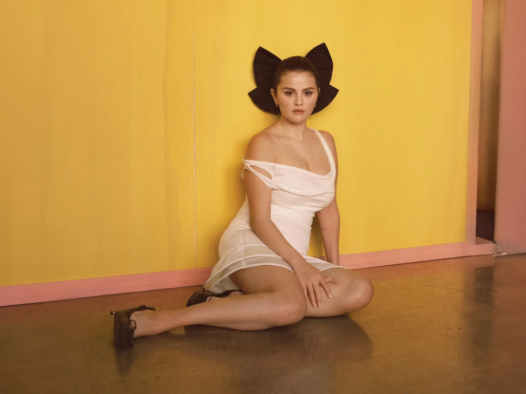 Молодая Селена Гомес сидит на полу у стены