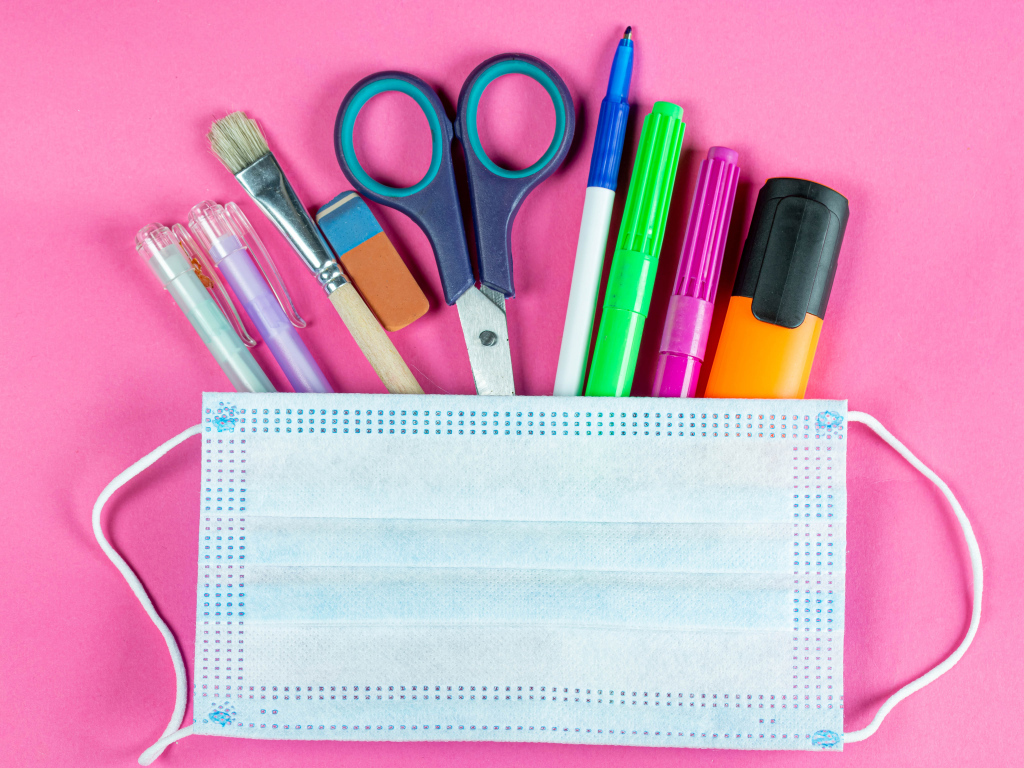 Канцелярские предметы и медицинская маска на розовом фоне