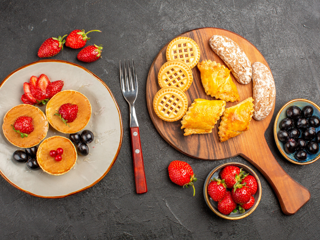 Печенье и оладьи на столе с ягодами клубники и виноградом