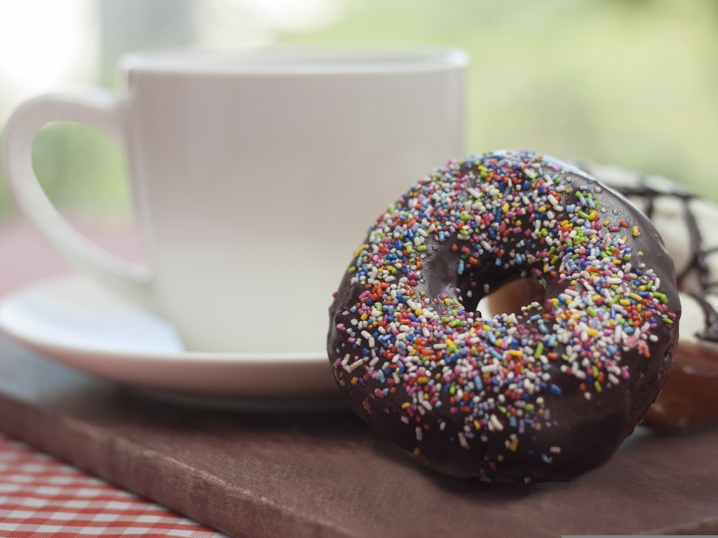 Донат с шоколадной глазурью и сладкой посыпкой на столе с чашкой чая