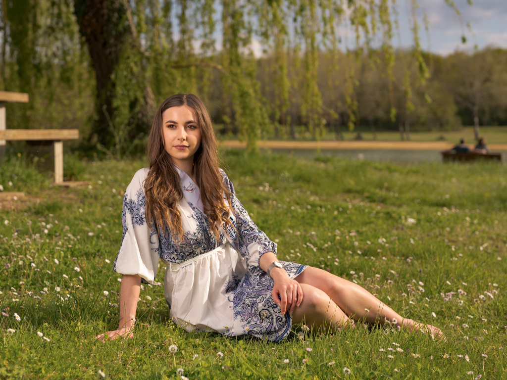 Красивая девушка в платье сидит на зеленой траве в парке