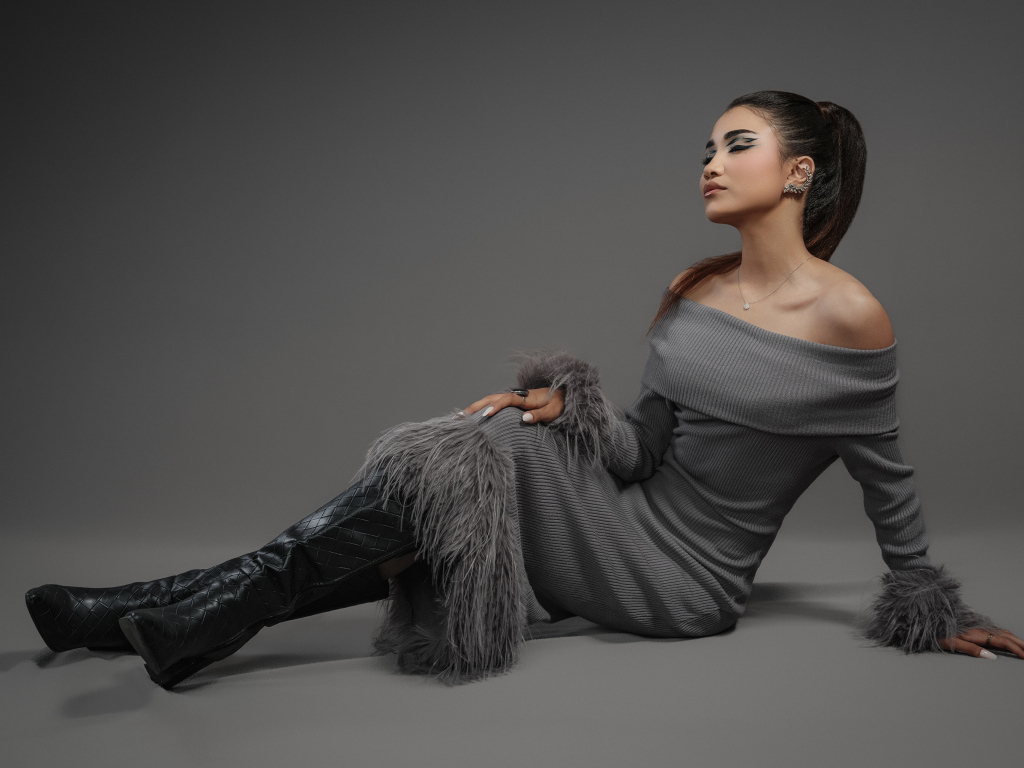 Девушка в платье и длинных черных сапогах на сером фоне