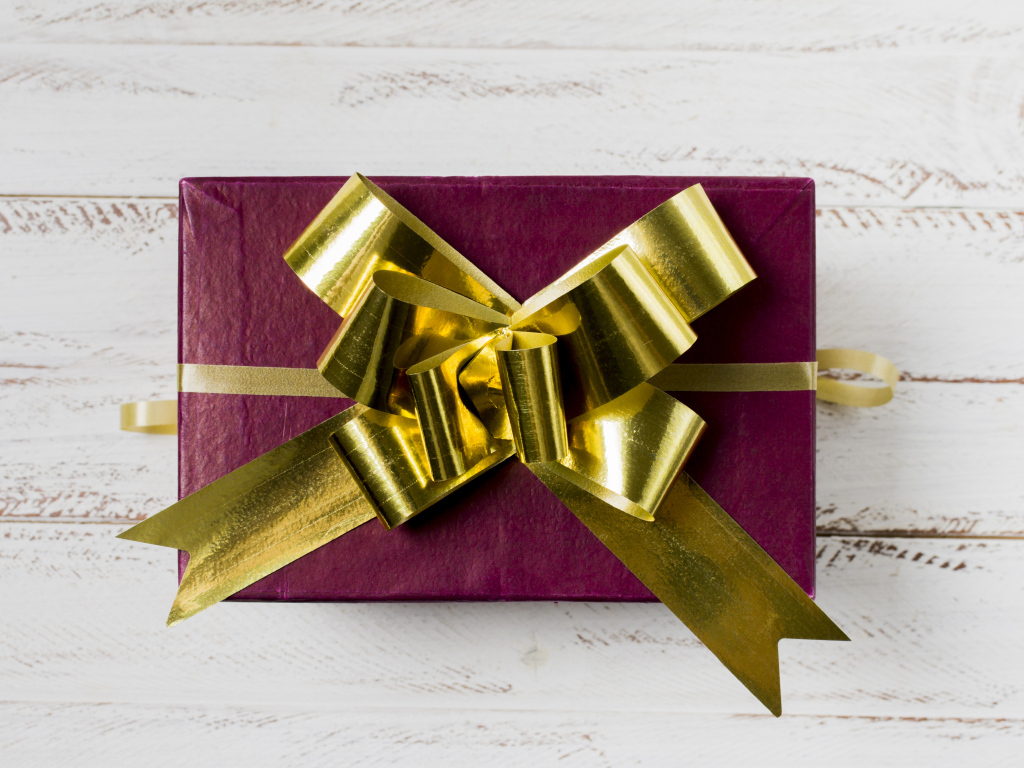 Красная коробка с подарком с золотым бантом на столе