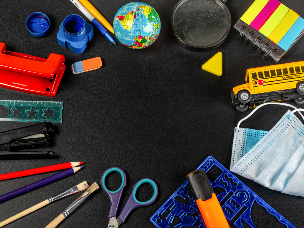 Канцелярские предметы, глобус и игрушечный автобус на черном фоне