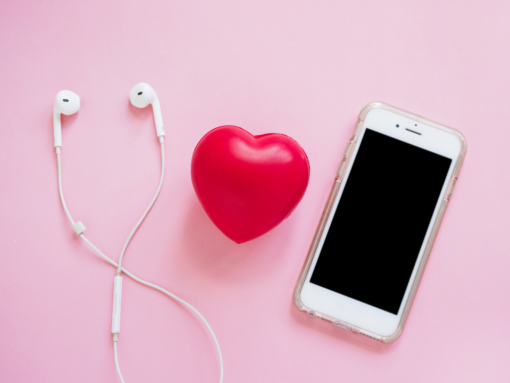 Телефон, наушники и красное сердце на розовом фоне