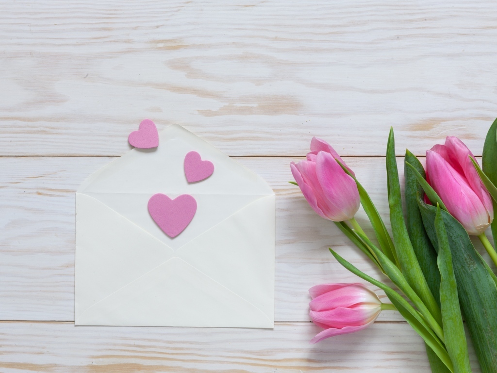 Розовые тюльпаны с конвертом с сердечками на деревянном фоне