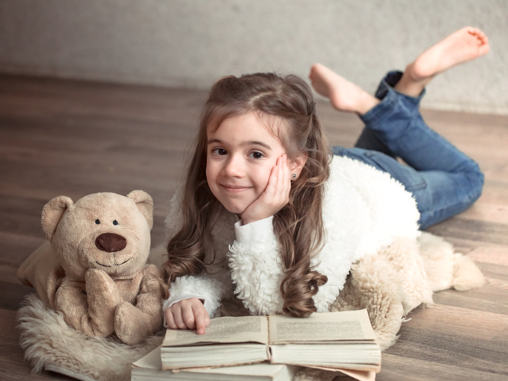 Девочка с медведем и книгой лежит на полу