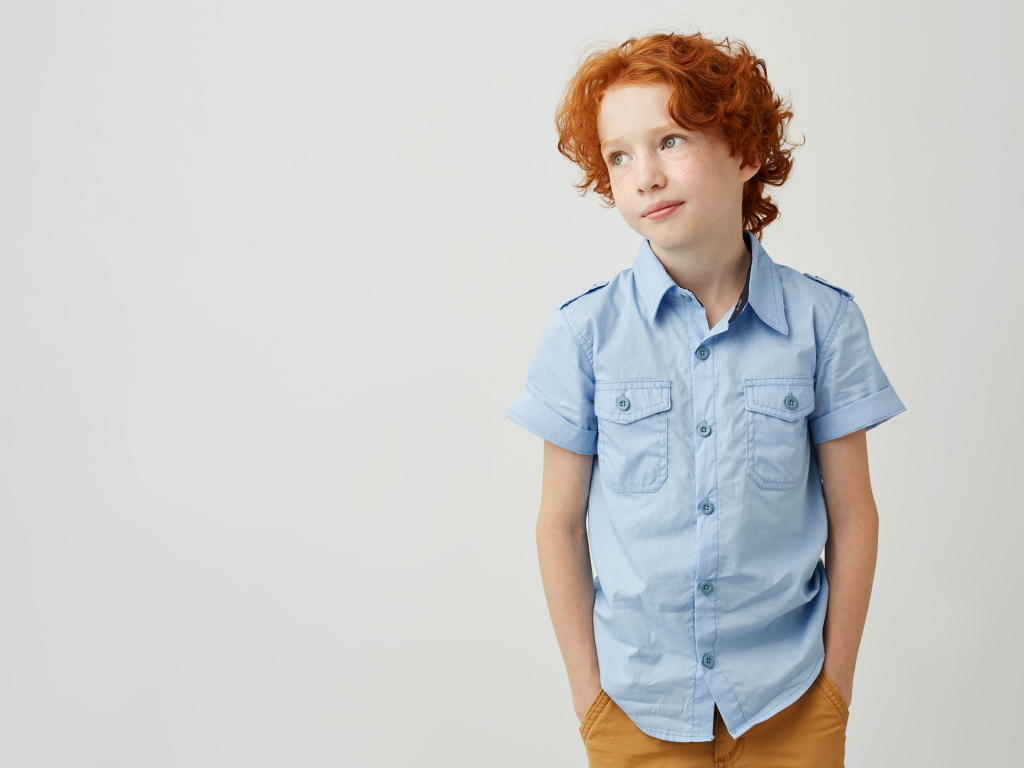 Рыжеволосый мальчик на фоне серой стены