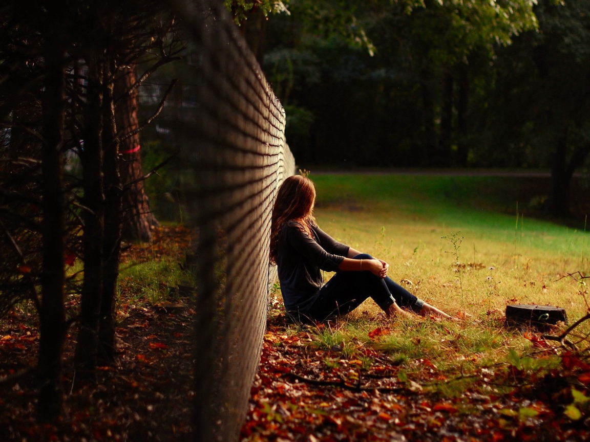 Девушка сидит у сетчатого забора на опушке леса