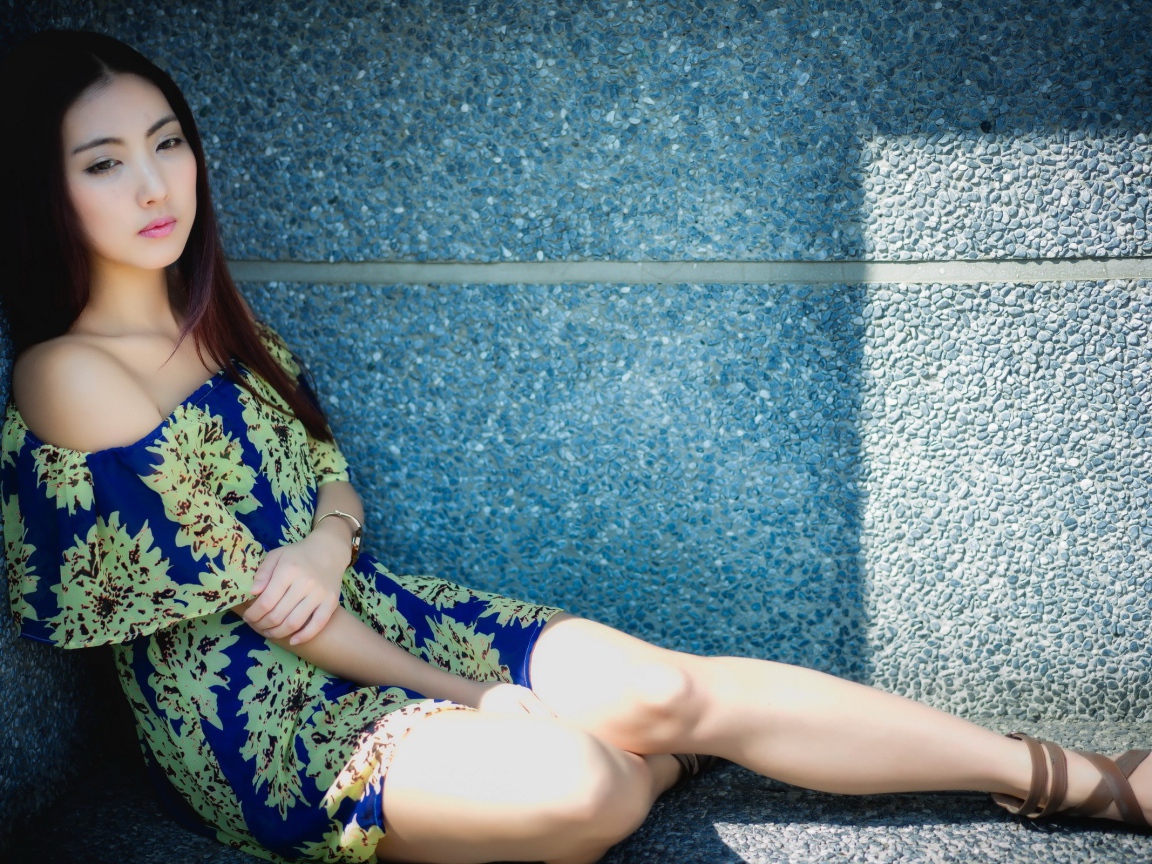 Девушка сидит в тени у гранитной стены