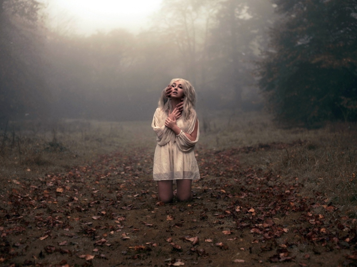 Блондинка в белом платье стоит на коленях среди леса