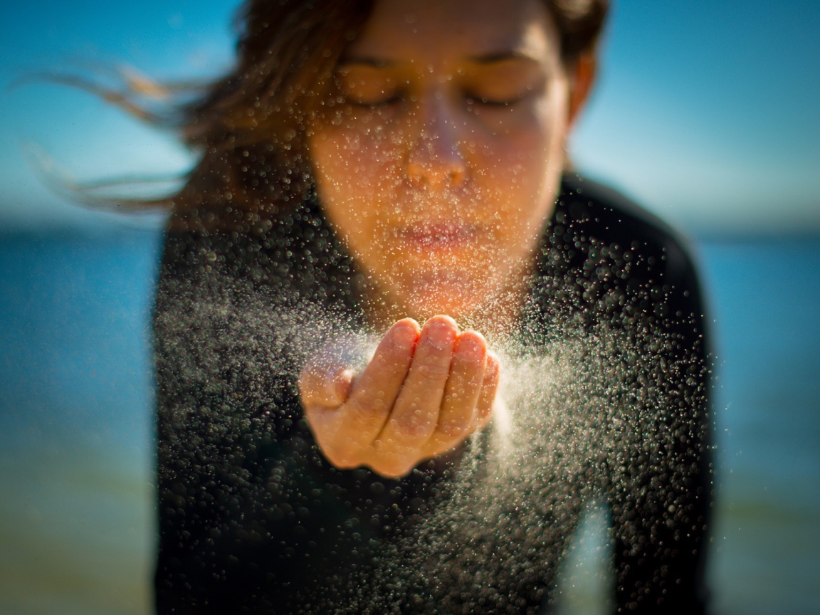 Девушка сдувает песок с руки