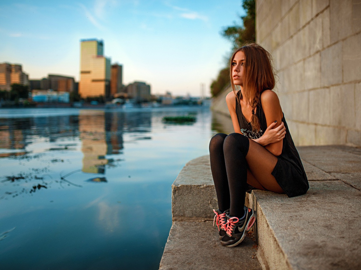 Девушка в кедах сидит на набережной