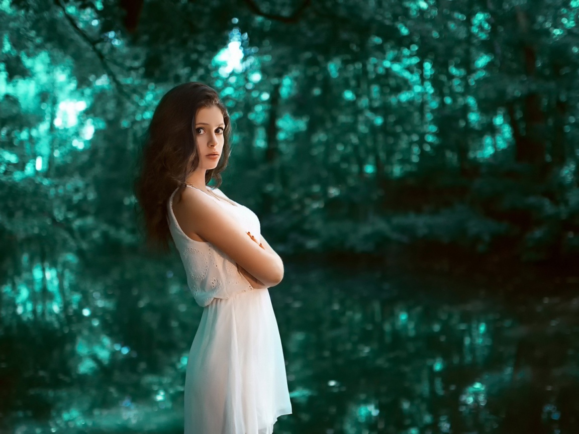 Девушка в белом платье стоит в зеленом лесу