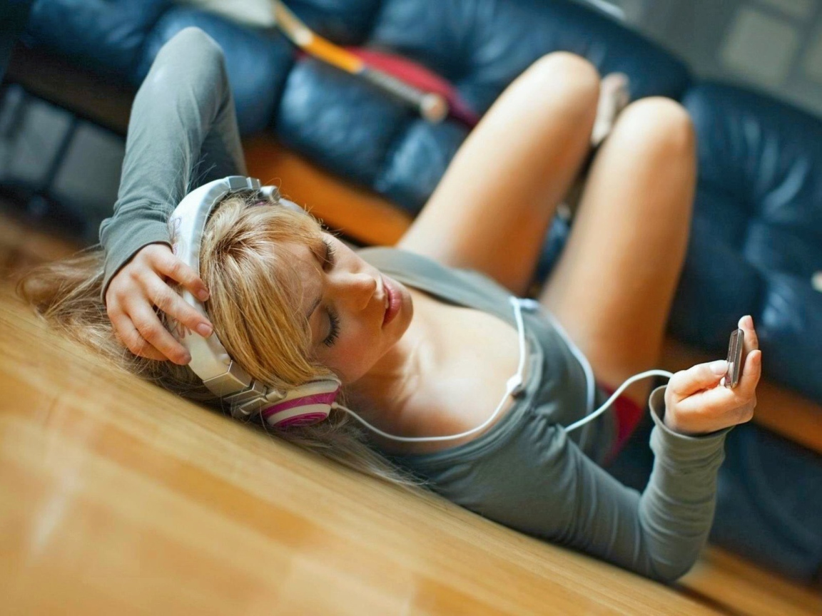 Девушка лежит на паркете и слушает музыку в наушниках