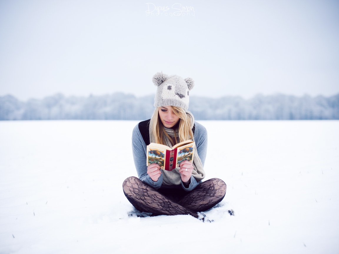 Девушка читает книгу сидя на снегу