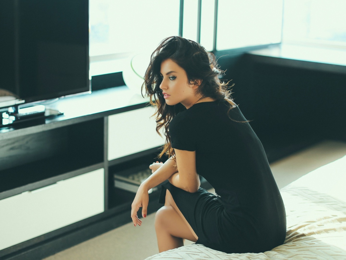 Девушка сидит на кровати перед телевизором