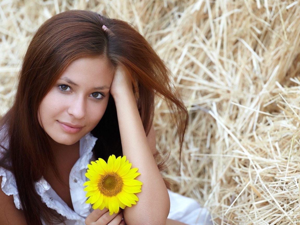 Девушка с желтым цветком сидит на сене