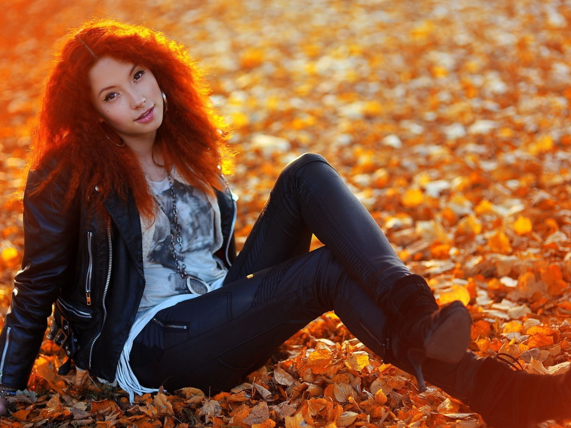 Рыжая девушка сидит на ковре из желтых листьев