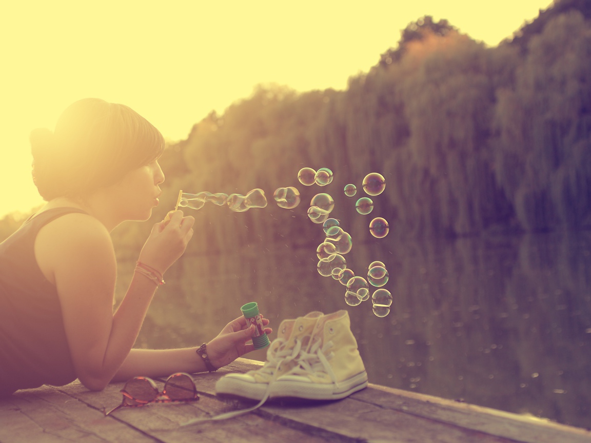 Девушка лежит на пирсе и играет с мыльными пузырями