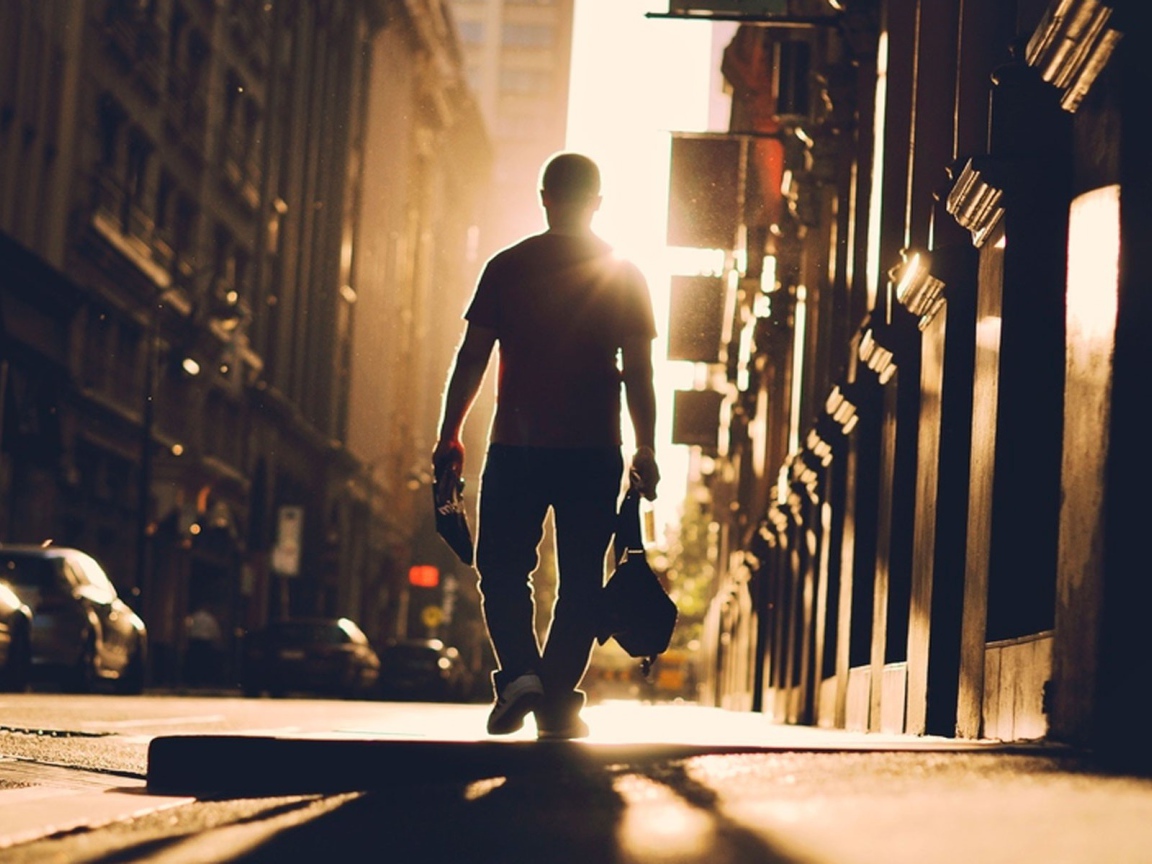 A man walks down the street towards the sun