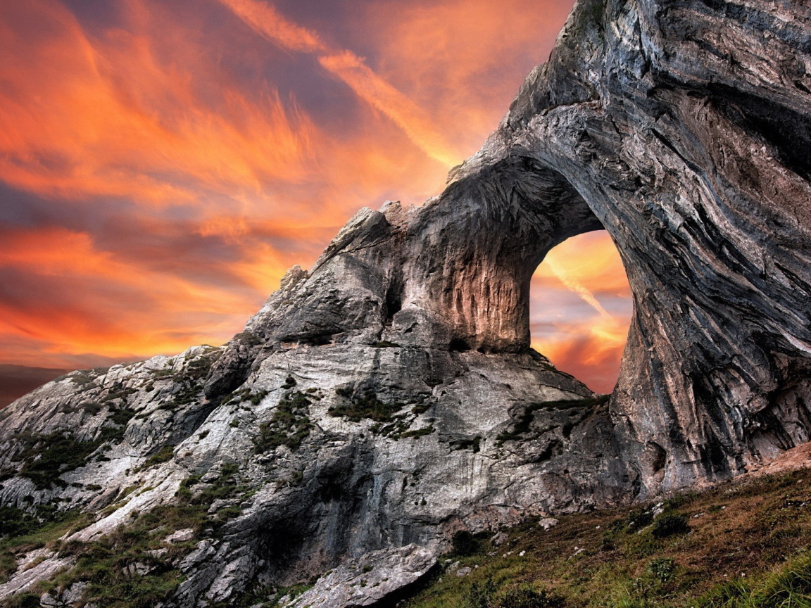 Овальный проход в скале на фоне оранжевого неба
