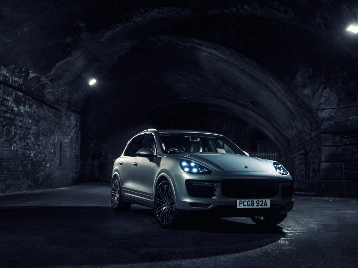 Серебристый автомобиль Porsche Cayenne в тоннеле с включенными фарами