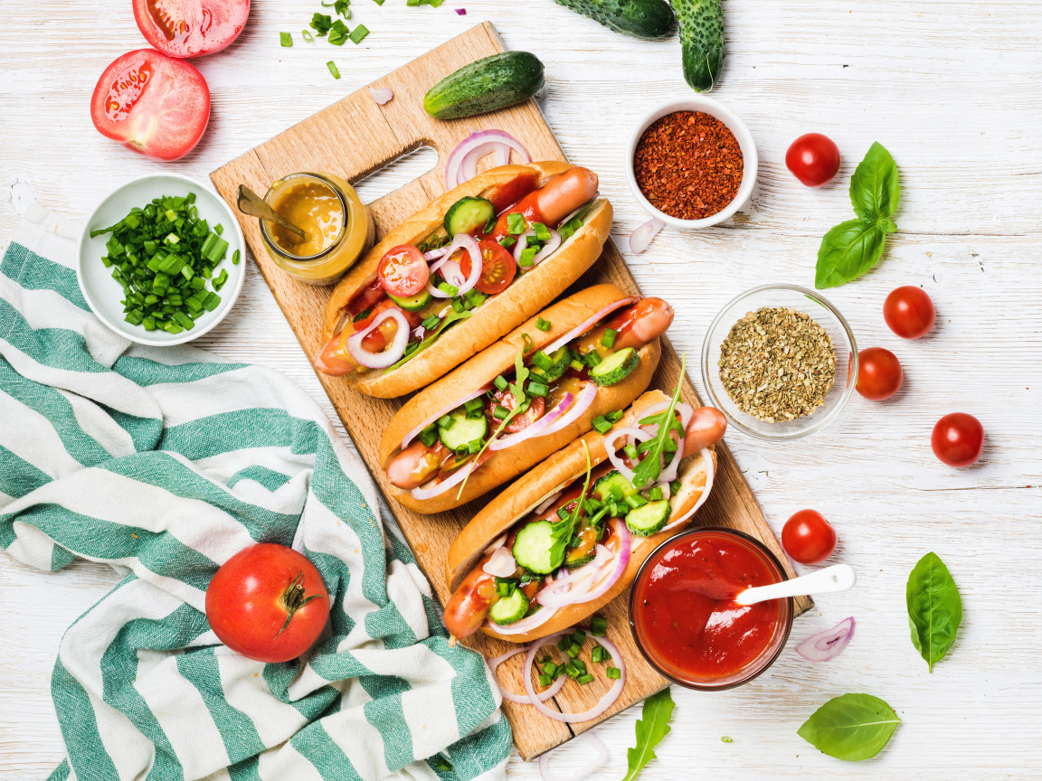 Аппетитные хотдоги на разделочной доске с овощами